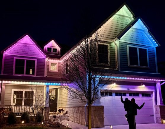 Two-story home at night with permanent lighting along every roofline, fading from pink to blue.