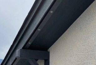 Daytime close-up of dark permanent lighting track tucked under the roof edge of a stucco home.
