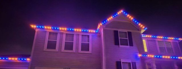 Two-story home lit in orange and navy blue along every roofline for game day.