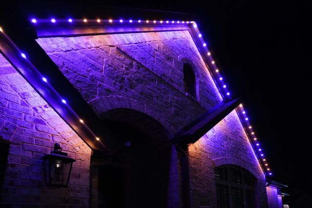 Close-up of a stone gable and arched entry washed in purple light from permanent lighting along the roof edge.