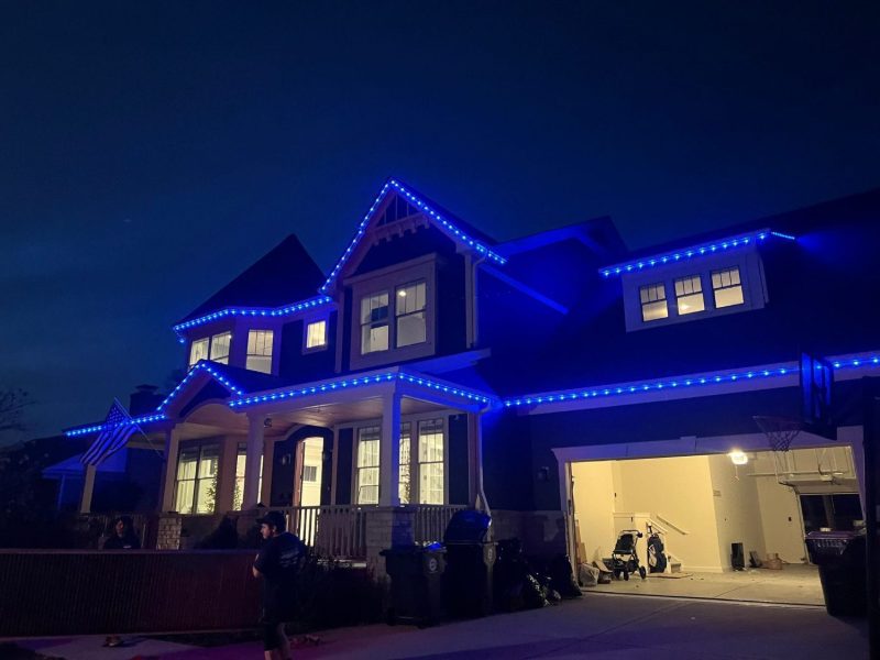 Two-story home with blue permanent lighting along the roofline and porch at night.