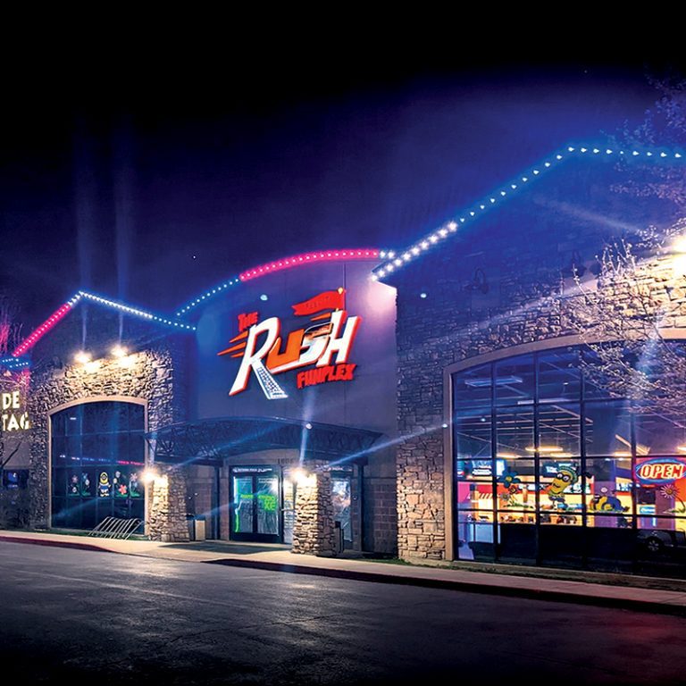 Retail storefront with blue and red lighting along the roofline at night.