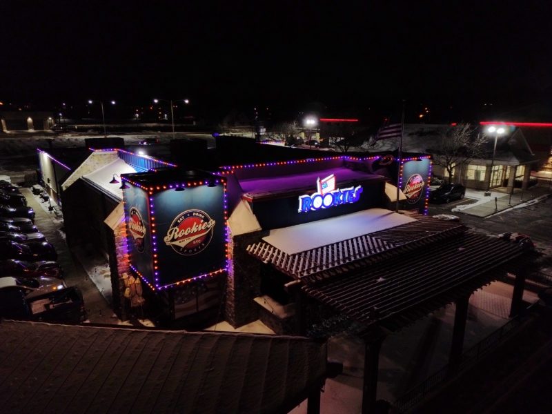 Aerial view of the Rookies sports bar building lit in purple and red at night.