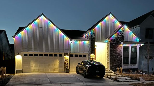 Board-and-batten home with rainbow permanent lighting along the gables at dusk, a black car in the driveway.