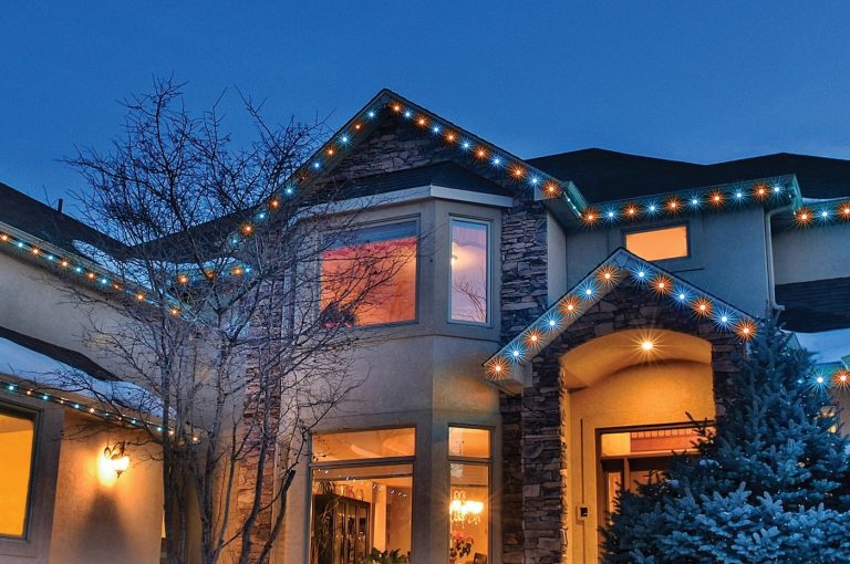 Two-story stone home with multicolor lighting along the roofline at night.